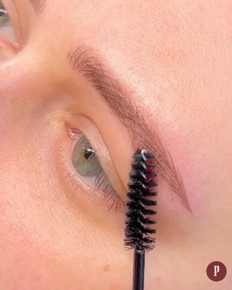 Nano feathering brow tattoo — fresh hair-strokes being groomed with a spoolie