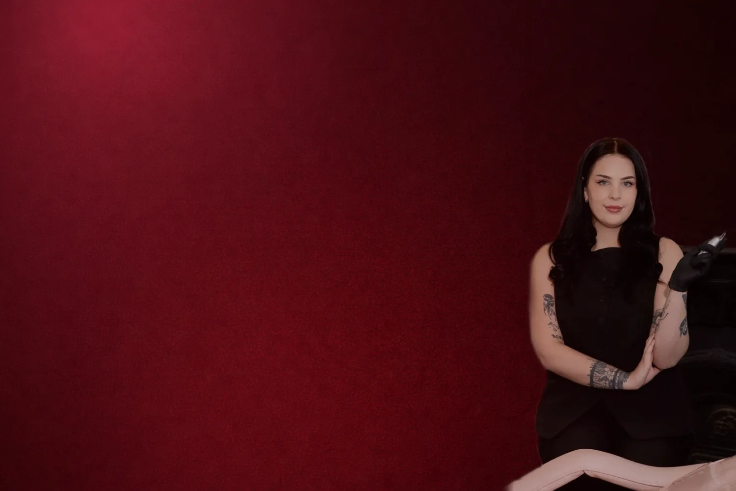 Kirra — staff artist and founder at Pixi Cosmetic Studio, seated with a tattoo machine against a deep burgundy velvet backdrop